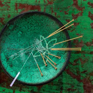 green ceramic Asian Bowl with needles for acupuncture on an old green paint wooden board
